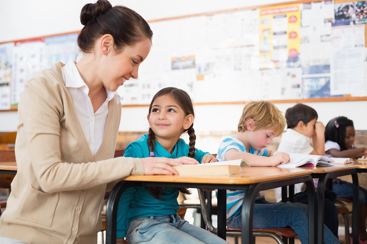 Pretty teacher helping pupil in classroom at the elementary school