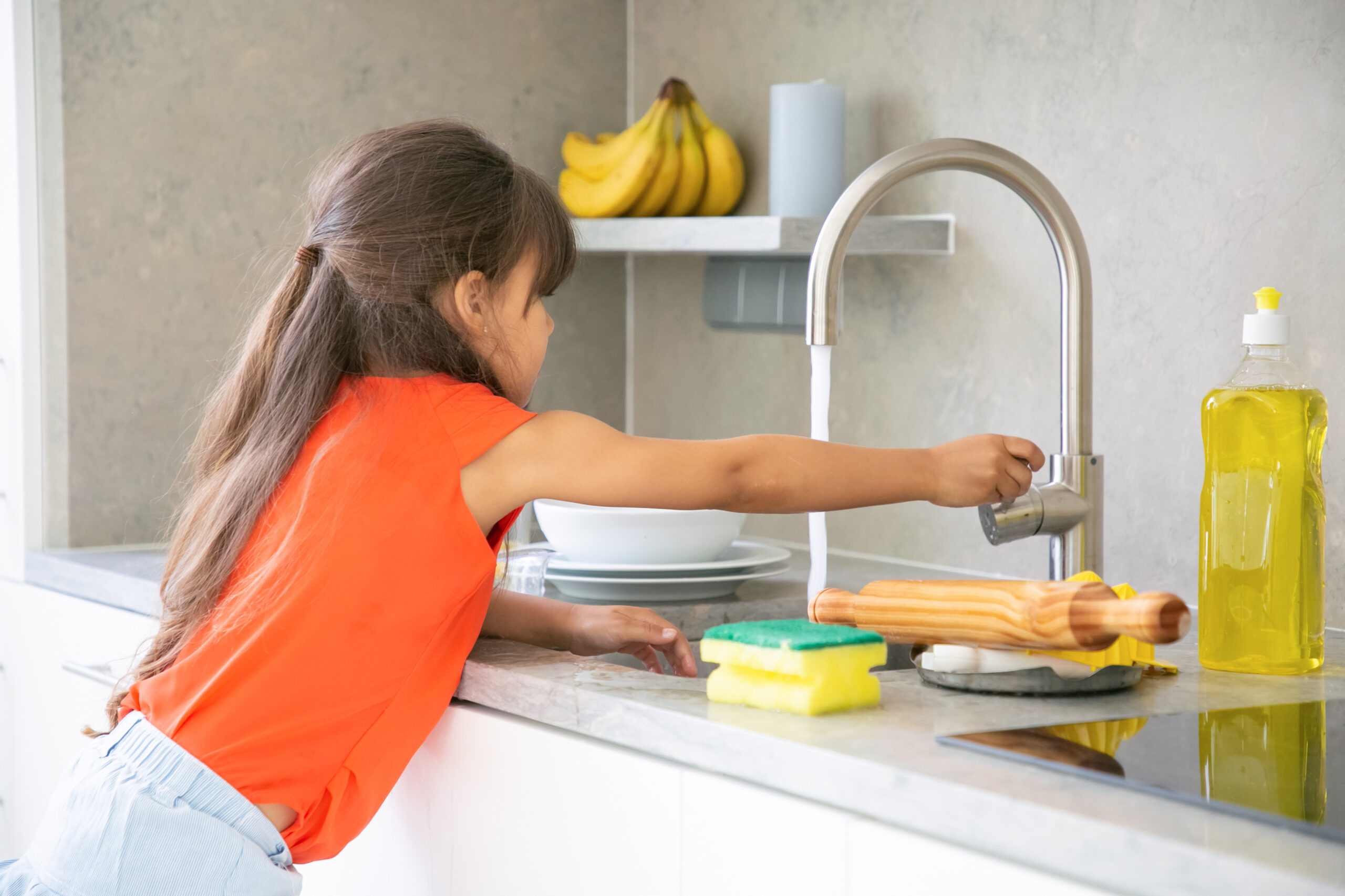 Cute little girl washing dish in kitchen by herself