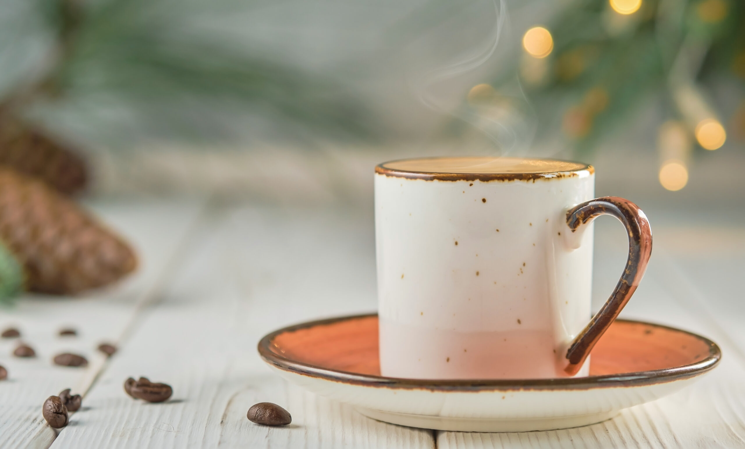 Cup of coffee with natural steam on a white wooden table, selective focus. christmas background with copy space. hot coffee drink concept. christmas tree with a garland on the table. new year concept